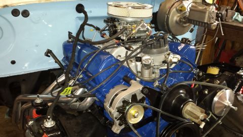 1978 Ford Bronco - A close-up view of a blue Ford V8 engine installed in a vehicle, featuring a chrome air cleaner, a carburetor, and exhaust headers. The eng…