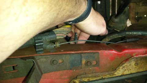 1991 Buick Reatta - A hand manipulates wiring and components within a red engine bay, with a black hose visible.