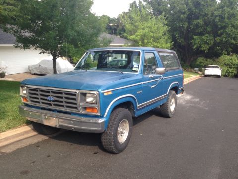 1984 Ford Bronco - Blue Ford Bronco parked on a residential street with trees and houses in the background.