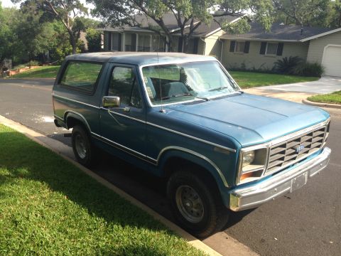 1984 Ford Bronco - This blue Ford Bronco is parked curbside on a sunny day in a neighborhood.