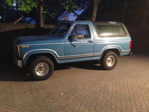1984 Ford Bronco - Side view of a blue Ford Bronco parked on brick pavement at night.