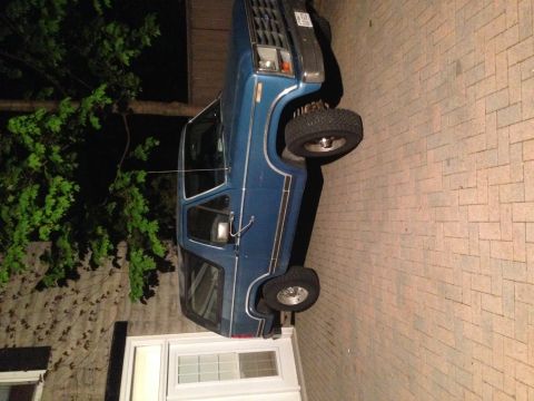 1984 Ford Bronco - A blue SUV is parked on a brick driveway at night, with a house and tree nearby.