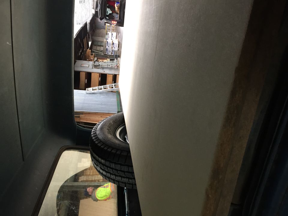 Spare tire mounted in cargo area of a vehicle, with a view of a workshop or storage area through a window