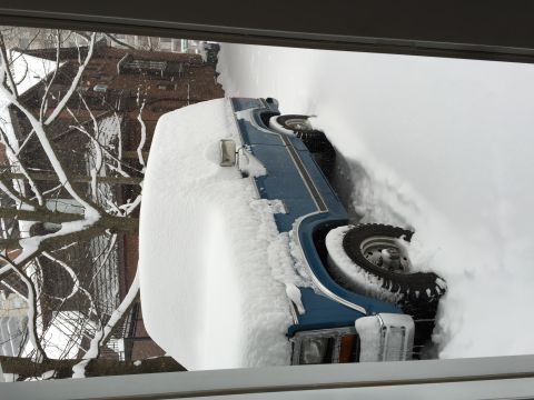 1984 Ford Bronco - A blue SUV is heavily covered in snow, with only parts of its body and tires visible.