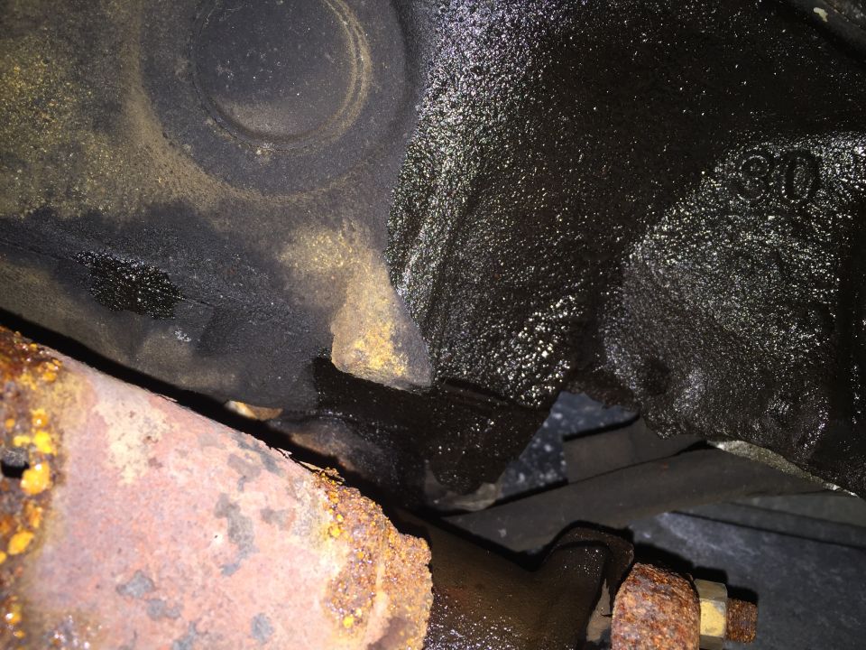 Close-up of oily engine block casting and rusty exhaust pipe