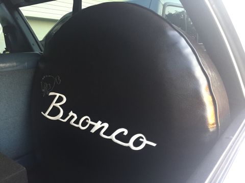 1995 Ford Bronco - Spare tire cover the iconic Bronco logo and script, seen inside a vehicle.