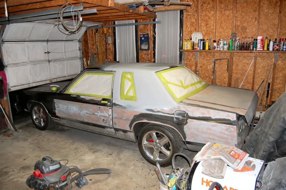 car in garage with body filler and masking tape on windows, looks like a 1985 Mercury Grand Marquis
