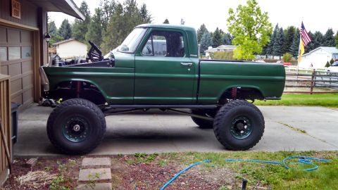 1967 Ford F-250 - A modified green pickup truck sits parked on a driveway, its lifted suspension and oversized tires.