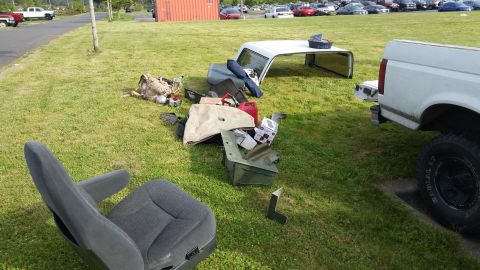 1993 Ford Bronco - Parts from a 1993 Ford Bronco are laid out on the grass, including a seat, doors, and roof section.