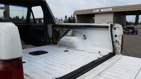 1993 Ford Bronco - Interior view of a white pickup truck bed, with a car wash visible in the background.