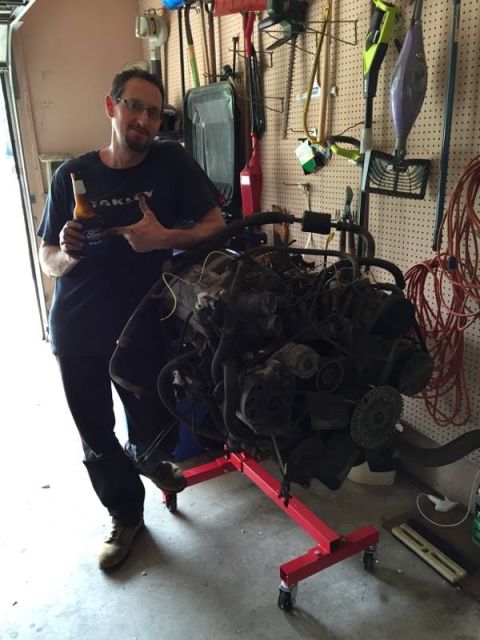 1990 Ford Bronco - A man poses with a V8 engine, which is mounted on a red engine stand in a cluttered garage.