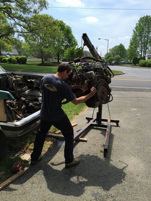 1990 Ford Bronco - A mechanic works on removing an engine from a vehicle using an engine hoist.