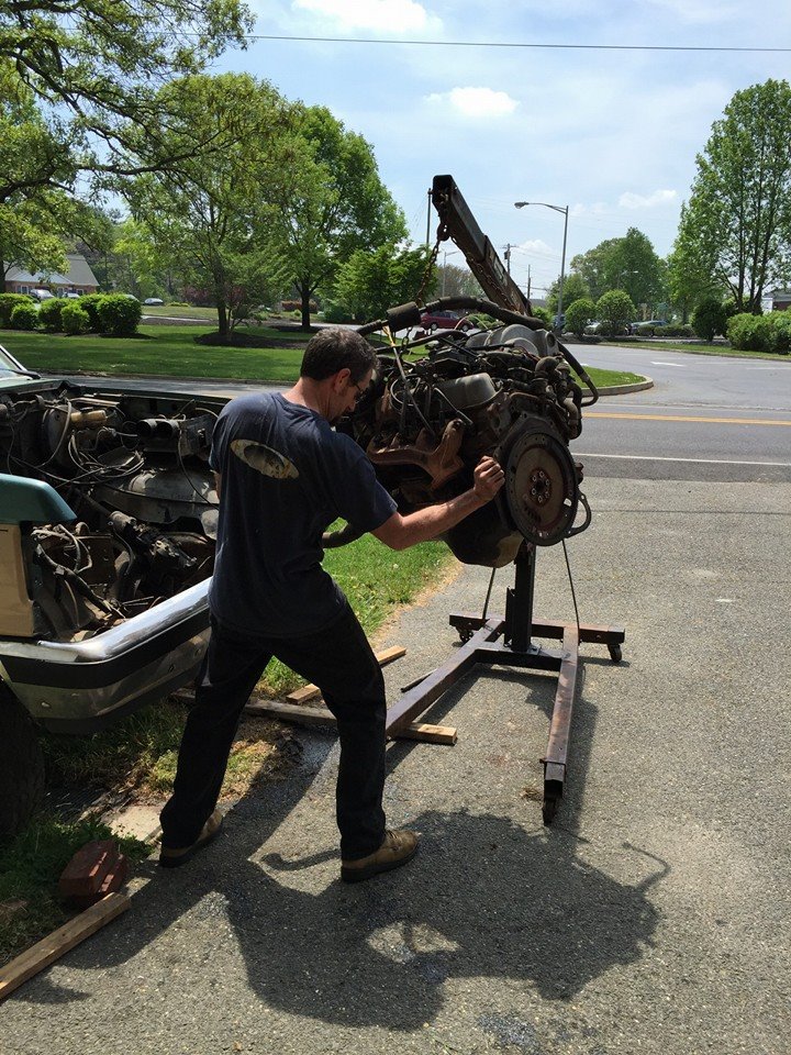 Man removing engine from a car with an engine hoist; car hood is open