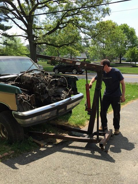 1990 Ford Bronco - Engine removal in progress on a green and tan truck, with a hoist positioned to lift the powertrain.