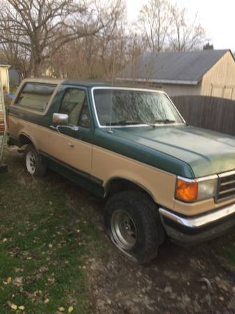1990 Ford Bronco - This two-tone Ford Bronco is parked outdoors with a flat tire on the front passenger side.