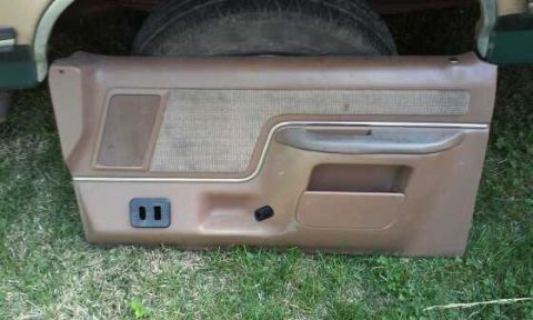 1990 Ford Bronco - A brown car door panel with a textured insert and chrome trim is shown, with a tire visible in the background.