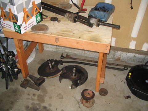 1989 Ford Bronco - Various automotive parts are laid out on a workbench and the floor, suggesting a repair or rebuild project.