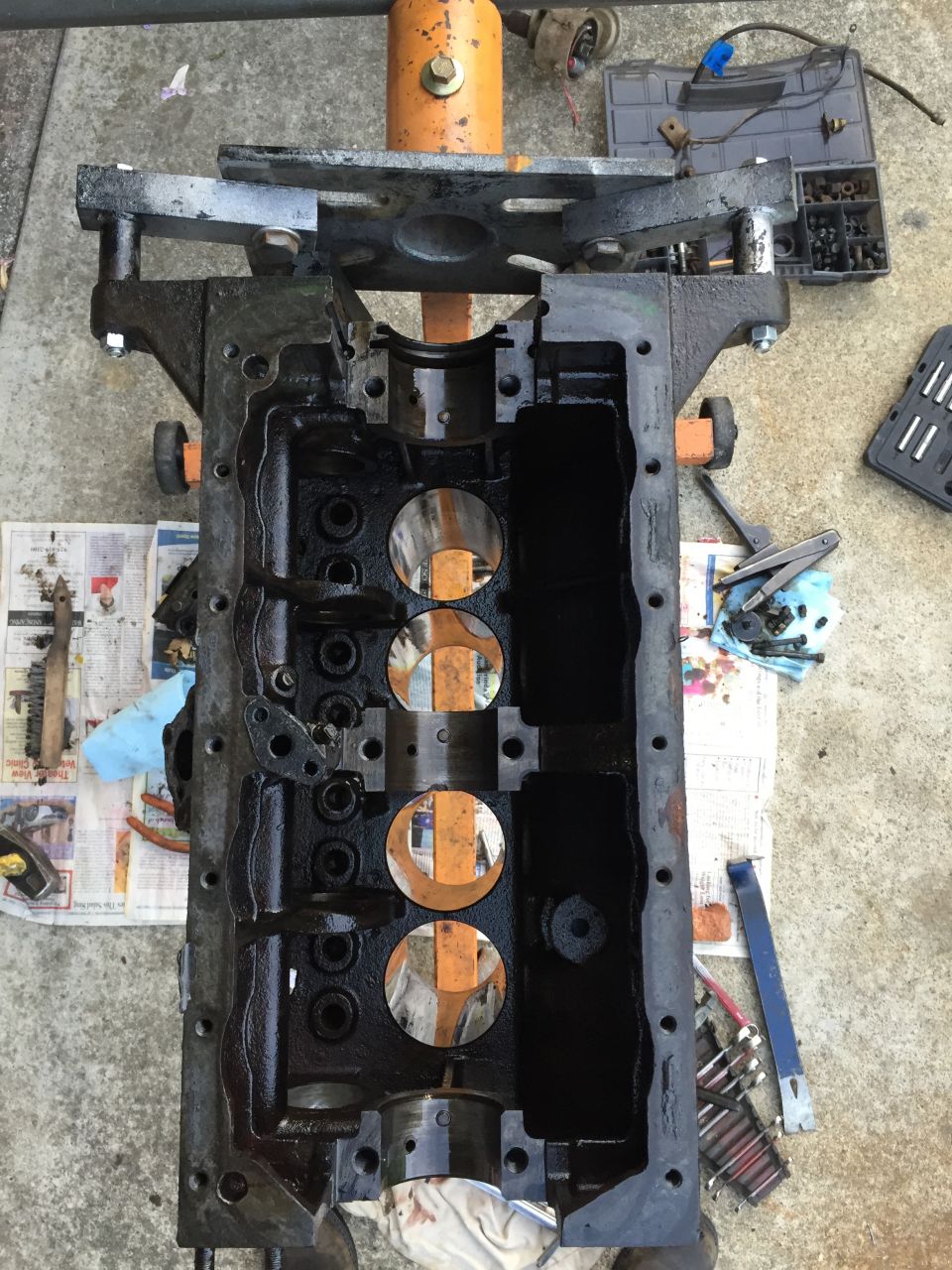Engine block disassembled and mounted on an orange engine stand, with tools and parts scattered around