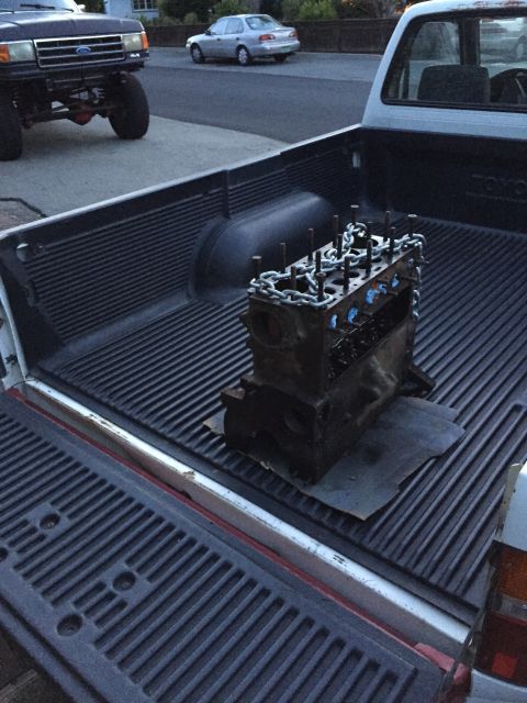 1946 Jeep Willys - Engine block being transported in the bed of a pickup truck, with other vehicles visible in the background.