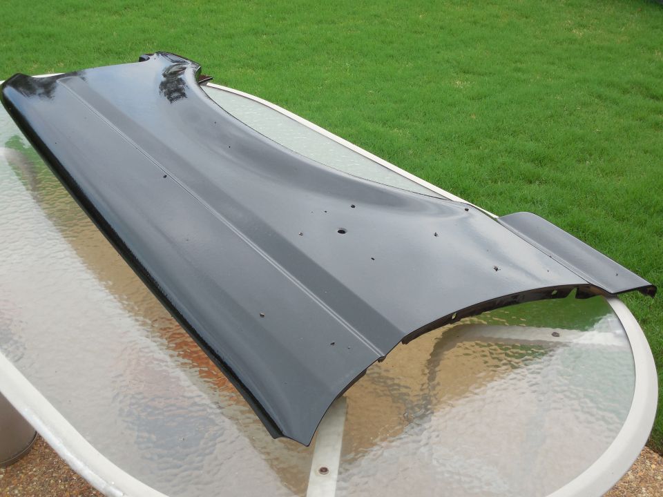 Black car fender with some dents and holes, resting on a glass-top table outdoors