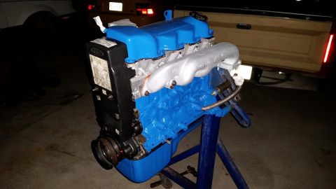 1985 Ford Escort - Engine assembly on a stand, painted blue with a silver intake manifold. A label with text is visible on the black component.