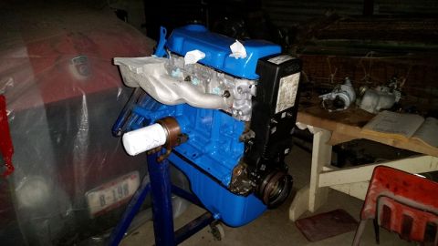 1985 Ford Escort - Engine on a stand, possibly undergoing restoration or rebuild. A red vehicle is in the background.
