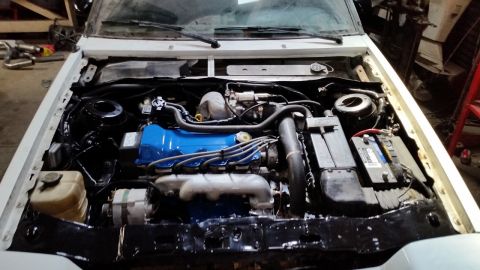 1985 Ford Escort - The engine bay of a car is shown with the hood open, revealing the engine and surrounding parts.