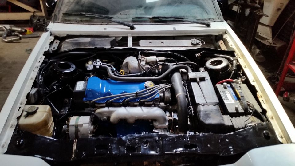 Car engine bay with blue valve cover and various hoses and components