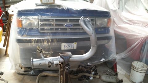 1985 Ford Escort - Front view of a blue Ford truck, likely from the late 1980s, partially covered by a plastic sheet.
