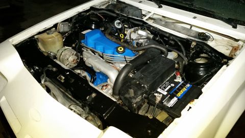 1985 Ford Escort - The engine bay of a white car, a blue valve cover and a SuperMotors watermark.