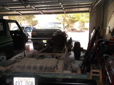 1979 Ford Bronco - The chassis of a vehicle is visible in the foreground, with a Ford pickup truck and an SUV in the background.