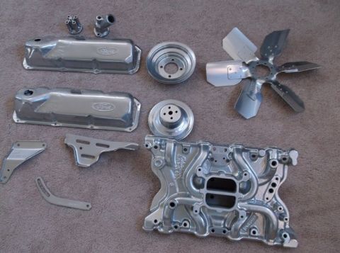 1979 Ford Bronco - Various engine components, including Ford-branded valve covers and an intake manifold, are arranged on a carpeted floor.