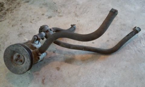 2004 Acura TL - A power steering pump with two dark hoses attached, resting on a concrete surface.