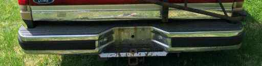 Rear bumper and tailgate of a red pickup truck with a chrome step and black trim