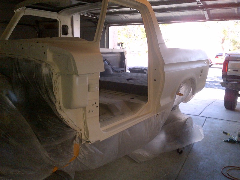 White 1978 Ford Bronco body undergoing paint preparation, covered in plastic sheeting