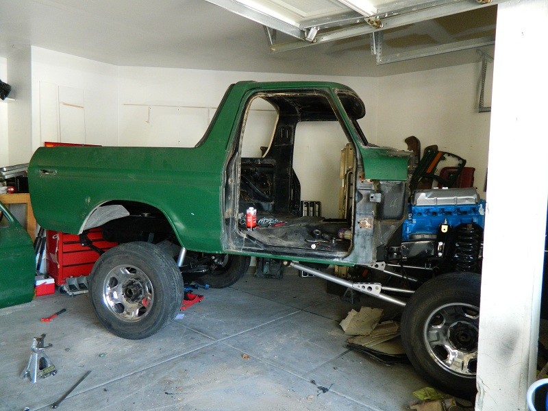 Green 1979 Ford Bronco side view, stripped down for restoration in a garage