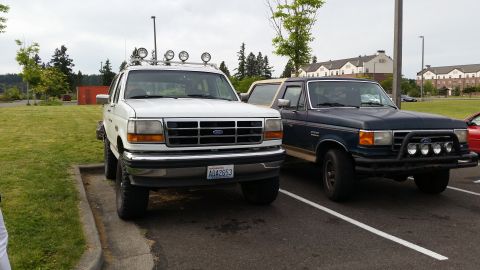 1993 Ford Bronco - Two Ford Broncos, one white and one dark blue, are parked in a lot.