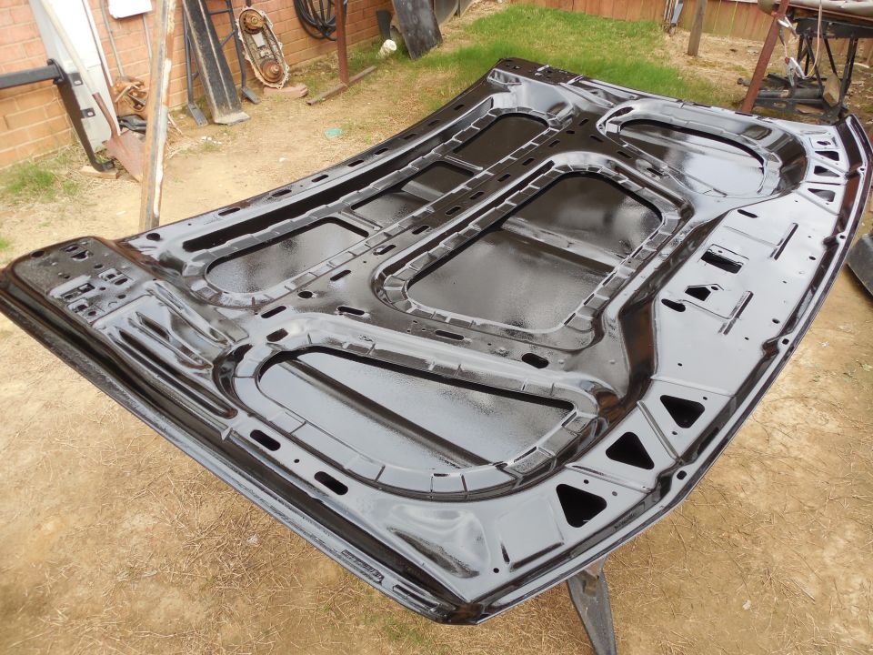 Freshly painted glossy black underside of a truck hood resting on stands in a dirt yard