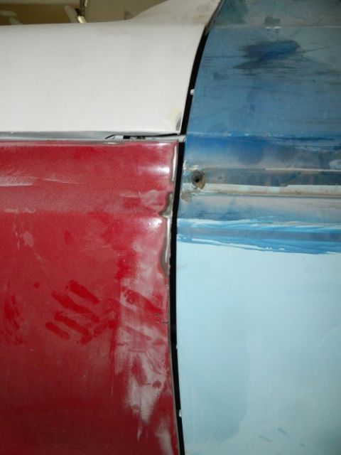1979 Ford Bronco - Detail of two car doors, one red and one blue, undergoing bodywork and painting.
