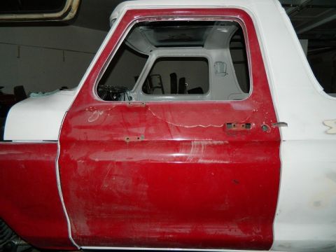 1979 Ford Bronco - Side view of a red and white Ford Bronco undergoing bodywork, showing a partially prepped door and fender.