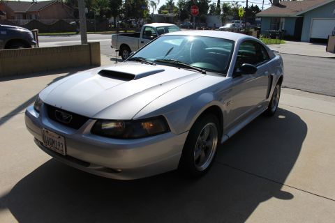 2002 Ford Mustang - A silver 2002 Ford Mustang coupe is parked in front of a house, with a pickup truck visible in the background.