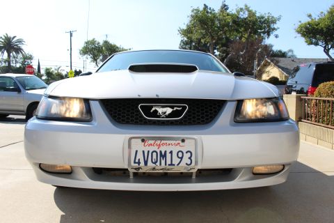 2002 Ford Mustang - A silver 2002 Ford Mustang is shown from the front, with its headlights illuminated and a California license plate.