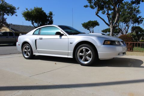 2002 Ford Mustang - This silver Ford Mustang GT is parked outside on a sunny day. The car has tinted windows and a hood scoop.