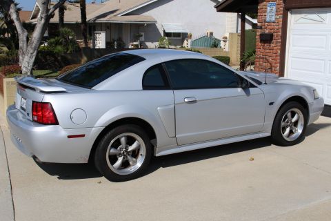 2002 Ford Mustang - Side view of a silver 2002 Ford Mustang parked in front of a garage.