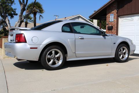 2002 Ford Mustang - A silver 2002 Ford Mustang is viewed from the side, parked in front of a brick garage.