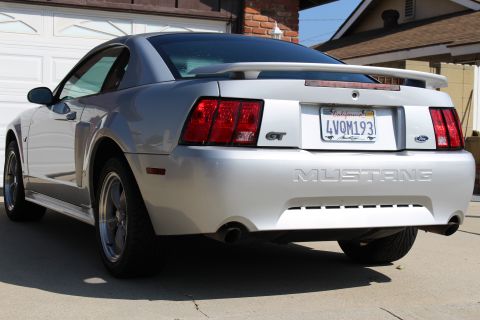 2002 Ford Mustang - Silver 2002 Ford Mustang GT with a spoiler and GT badging is parked in front of a garage.