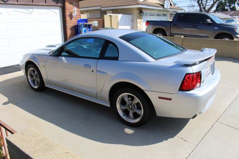 2002 Ford Mustang - Silver 2002 Ford Mustang coupe parked in front of a garage with a pickup truck in the background.