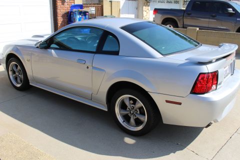 2002 Ford Mustang - A silver coupe is parked in a driveway with a pickup truck behind it.