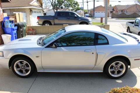 2002 Ford Mustang - Silver coupe parked in a driveway with a pickup truck behind it.