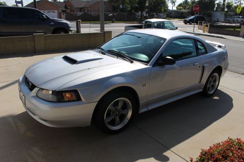 2002 Ford Mustang - A silver 2002 Ford Mustang GT is parked in front of a house, with a dark SUV in the background.